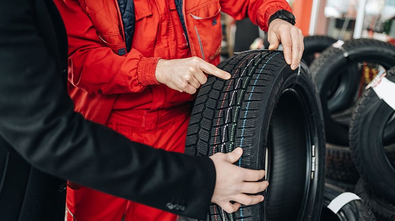 Young handsome customer after fueling his car on gas station looking for some good new winter tires. He is talking with salesman and asking him for advice. Credit: mladenbalinovac  iStock.com