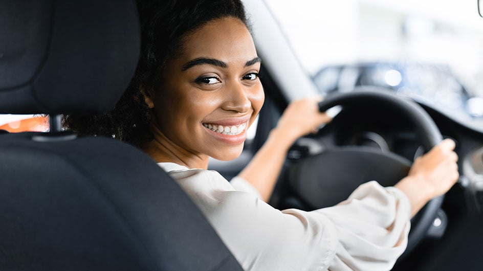 woman smiling with hands on steering wheel facing back seat of car
