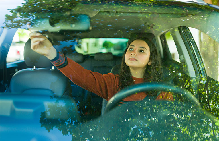 teenager wearing seatbelt and checking rearview mirror