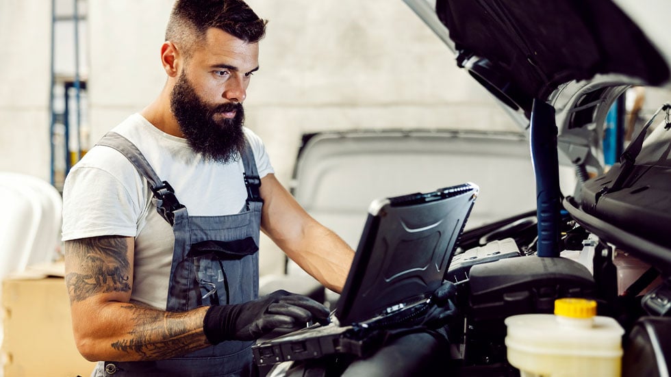 A mechanic diagnostic a problem with auto on laptop at workshop