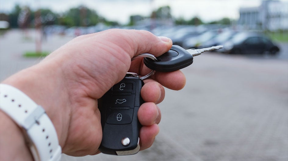 Man holds a car key in a parking lot with several cars. The concept of remote car opening and vehicle rental