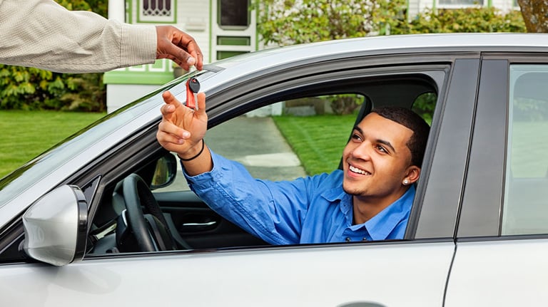man sitting in car driver's seat, being handed car key