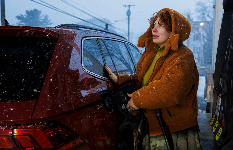 woman getting gas as snow falls