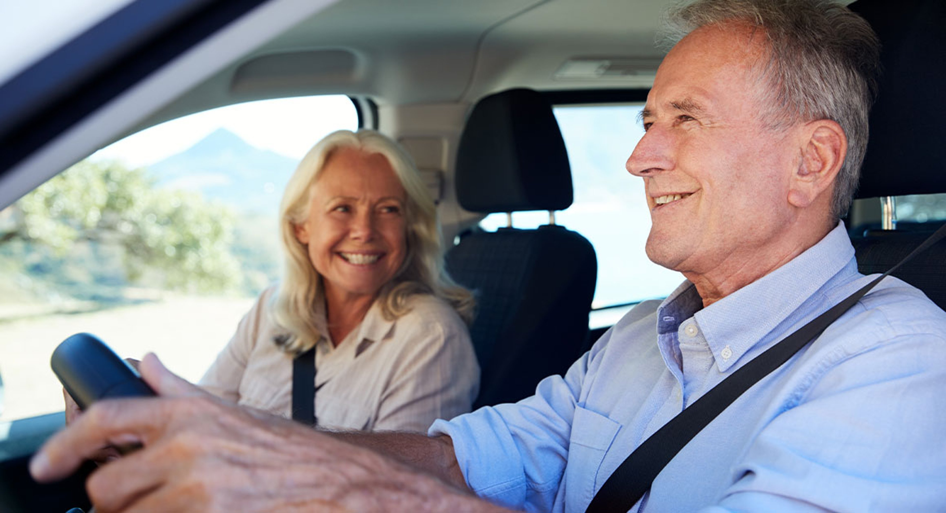 Senior white man driving car, his wife beside him in the front passenger seat, close up