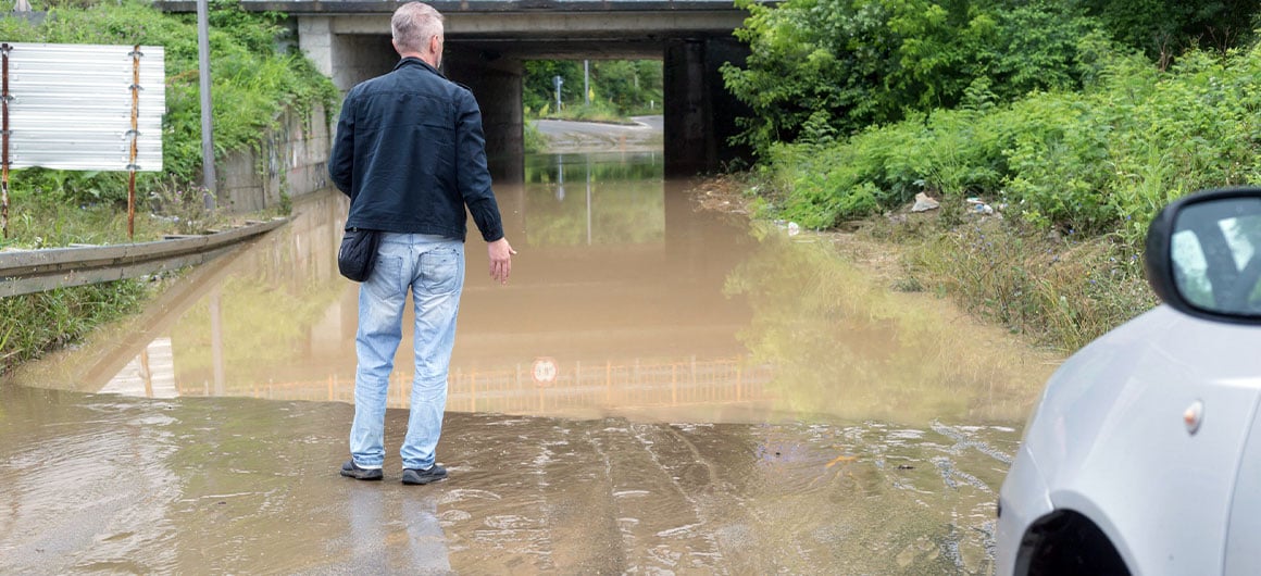 man standing outside of car looking forward at flood water