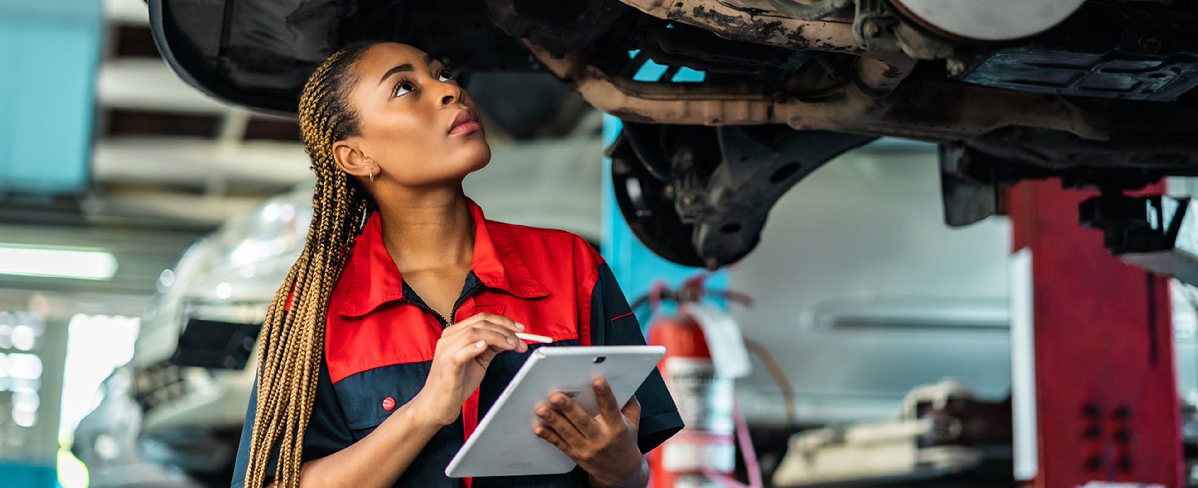 Engineer team checking under car condition on lifter in garage.Young auto mechanic in uniform is looking at camera and smiling examining car. Credit:anon-tae