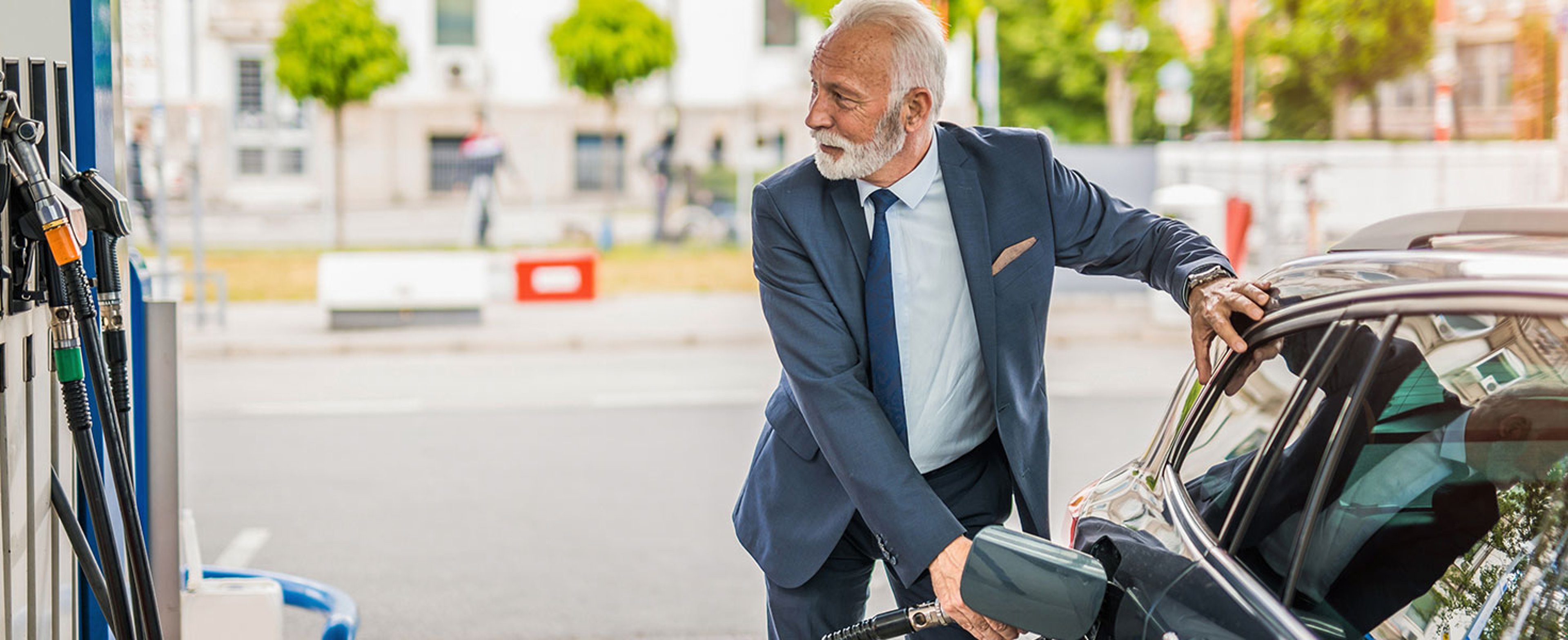 Senior businessman sipping fuel into his car tank at the gas station. Credit: DjelicS