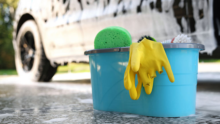 Car cleaning supplies and auto covered with foam outdoors Credit: Liudmila Chernetska
