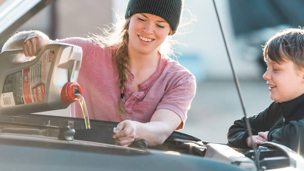 Woman pouring oil into car while little boy looks on