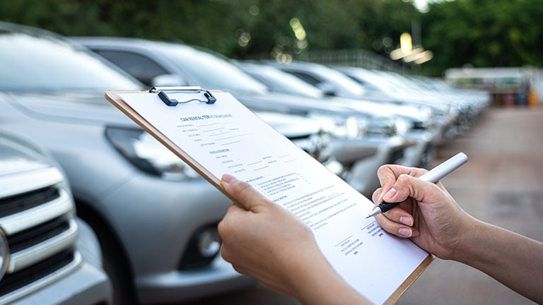 Action of a customer is signing on the agreement term of car rental service. Close-up and selective focus a human's hand with blurred background of cars in row. Business and transportation concept. by Nattawit