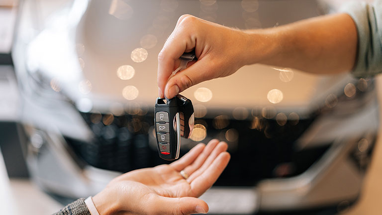 Close-up hands of unrecognizable dealer male giving new car key to customer man in business suit on blurred background of new auto in dealership office. Concept of choosing and buying car at showroom. by dikushin