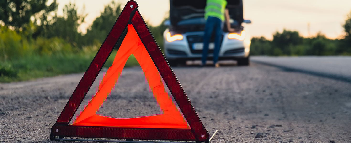 Broken silver luxury car emergency accident. Man driver installing red triangle stop sign on road. Sport automobile turned on blinkers technical problems on the road. Safety procedure when having vehicle broken down Credit: Anastasiia Yanishevska with istock