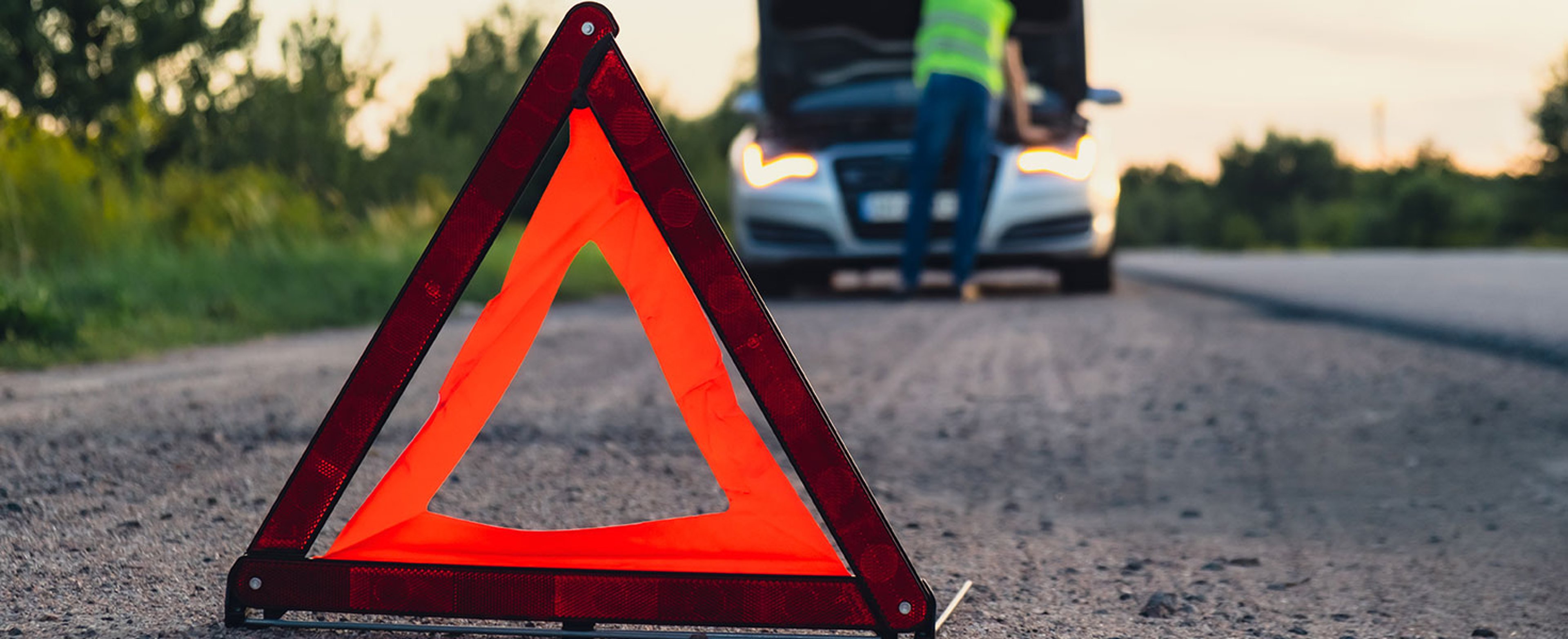 Broken silver luxury car emergency accident. Man driver installing red triangle stop sign on road. Sport automobile turned on blinkers technical problems on the road. Safety procedure when having vehicle broken down Credit: Anastasiia Yanishevska with istock