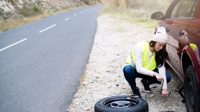 Middle-aged man refuels his red hatchback on a highway shoulder using a red gas can. Open trunk reveals luggage, indicating a road trip. Scene depicts a common roadside emergency where vehicle has run out of fuel. Driver, dressed casually, carefully pours gasoline into tank, highlighting importance of carrying emergency fuel on long trips. Credit:Julia Kozlov