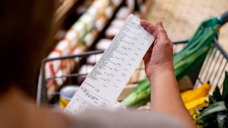 Close-up on a woman looking at a receipt after shopping at the supermarket - cost of living concepts
