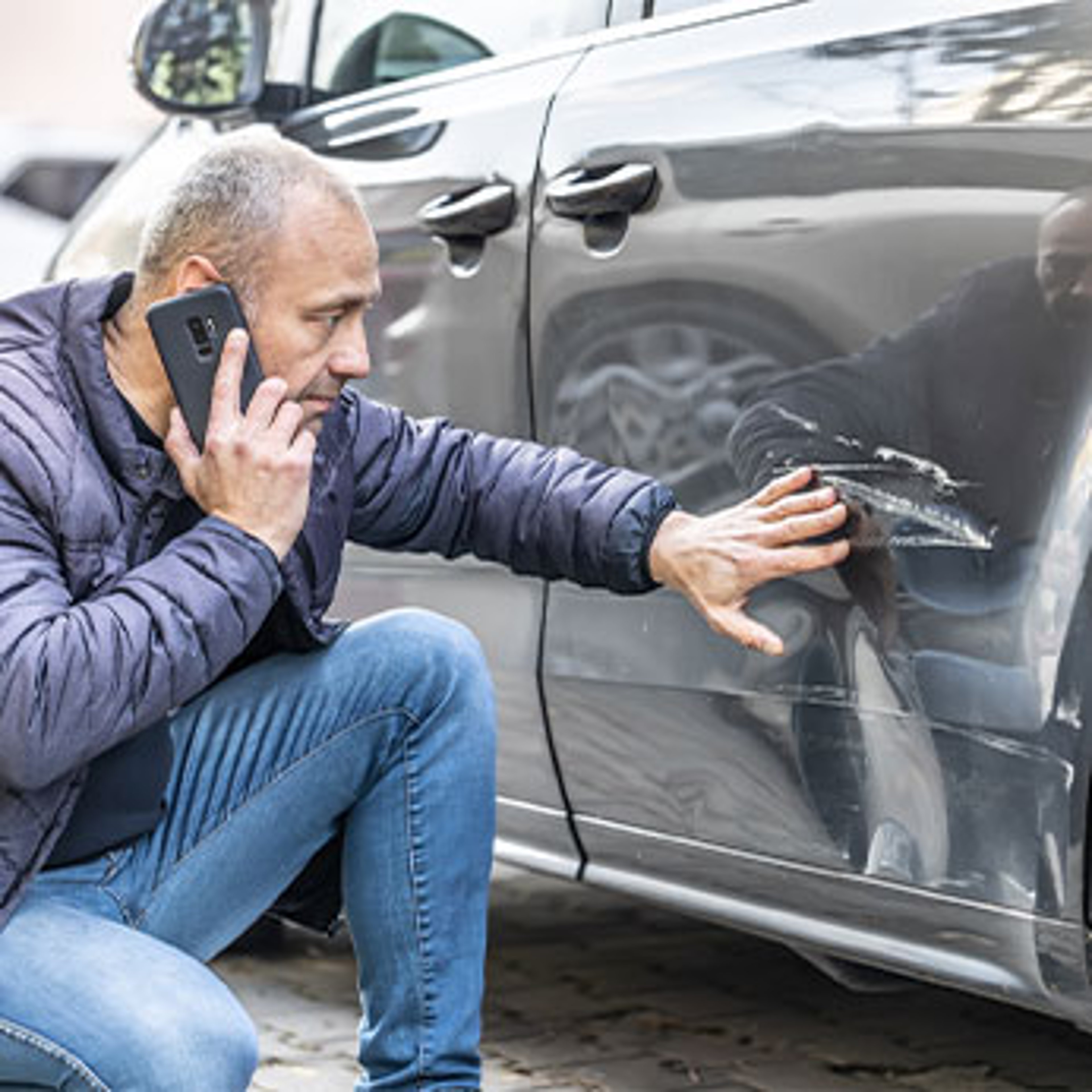 man looking at dent on his car while speaking on the phone