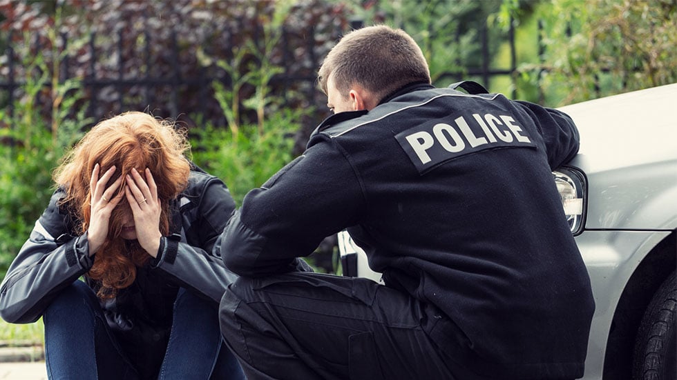 police officer speaking to person sitting on curb next to a car