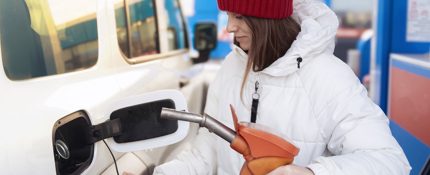 A woman in a white down jacket refueling her car at a gas station. She holds a gun in her hands to fill the car's gas tank Credit: Vladimir Razguliaev