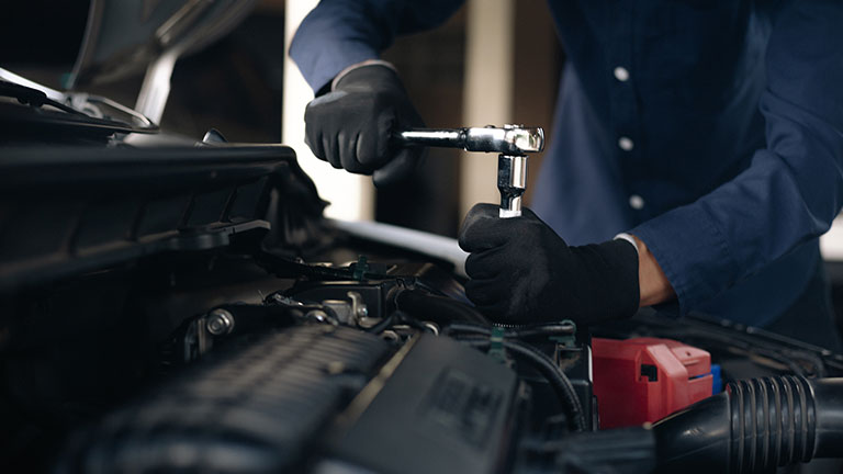 Male engineer repairing car with manager in background. Technologists is looking at motor vehicle in industry. Male and female professionals are representing teamwork in showroom. Credit:Morsa Images
