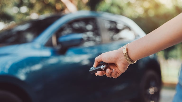 Close up hands woman pressing remote systems key near car for lock, unlock of blue hatchback car near street road driving. By Kiattisak