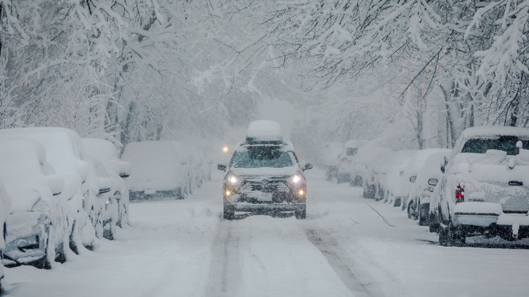 Front View of SUV Car driving through urban City during heavy Snowfall. Street, Cars and Trees covered in heavy Snow; Copyspace By christianthiel.net
