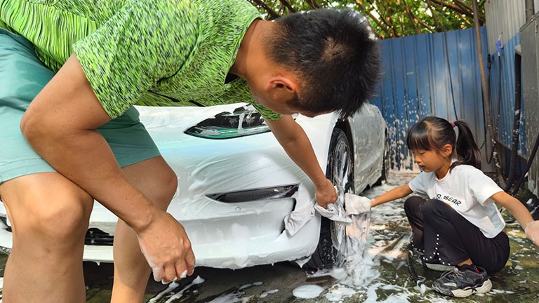 A 9-year-old girl is helping her father wash the car. They wash the car in a self-service car wash. They use a rag to spray foam on the car's sheet metal, and then rinse it with high-pressure water. Credit:Gins Wang
