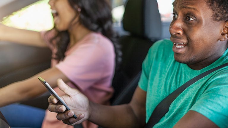 Young Black ethnicity teenager boy using holding smart phone while driving in car wearing seat belt distracted car accident crash. Credit: FangXiaNuo