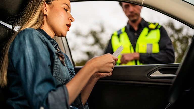 Young woman receiving a traffic ticket from a traffic cop inside car Credit:FG Trade Latin