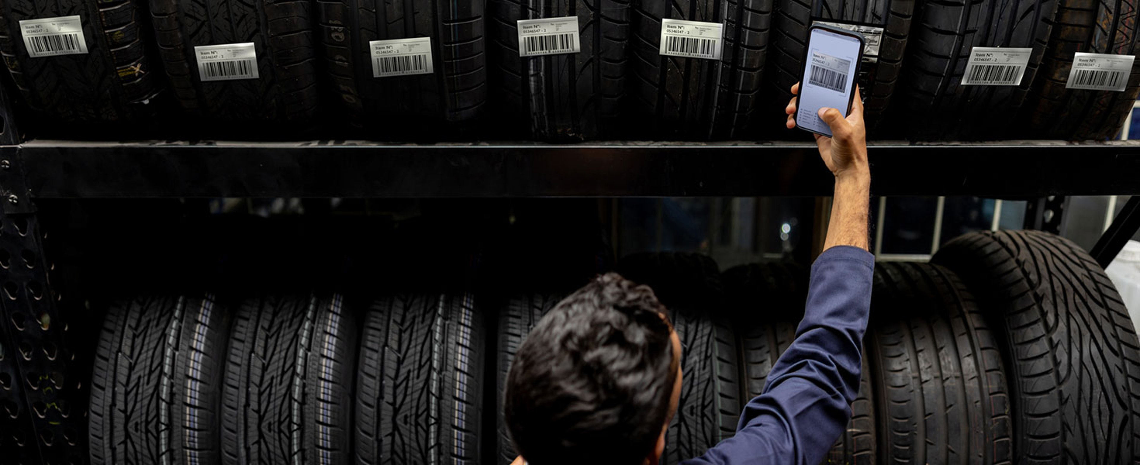 Latin American employee scanning a bar code on a tire at a garage shop using a cell phone Credit:andresr