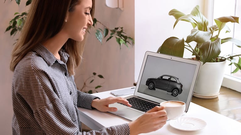 A woman using a laptop to buy a car at a table indoors.