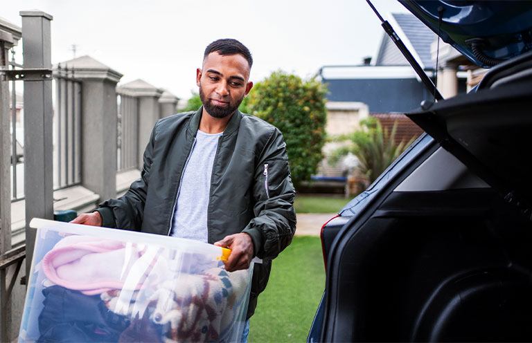 man placing storage bin in car trunk
