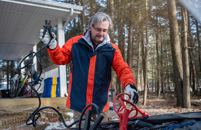 man attaching jumper cables to car battery