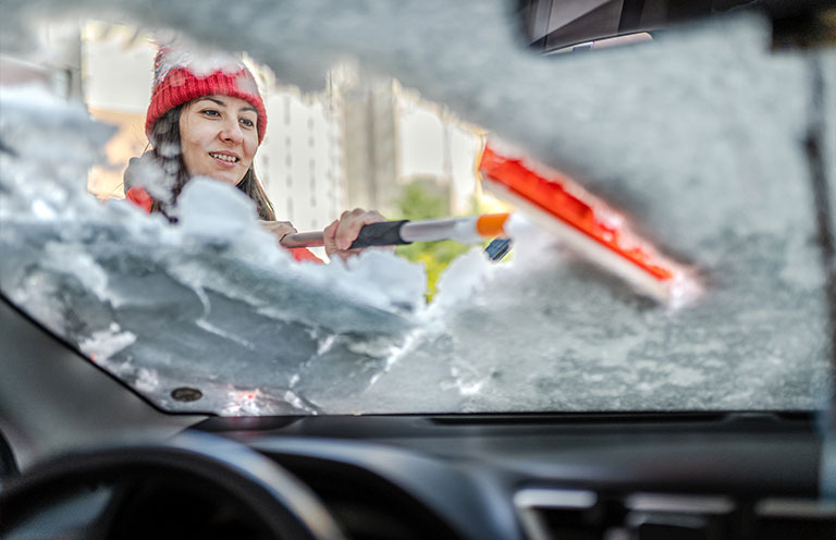 woman scraping off snow and ice on car windshield