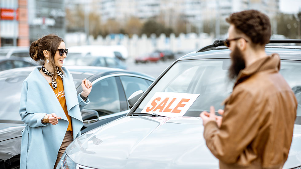 Man and woman looking at car with a For Sale sign on windsheild