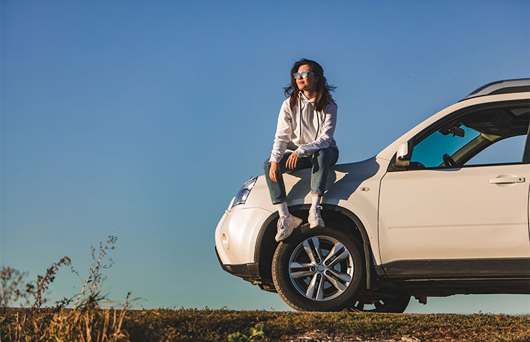 woman sitting on white car, blue sky in the background