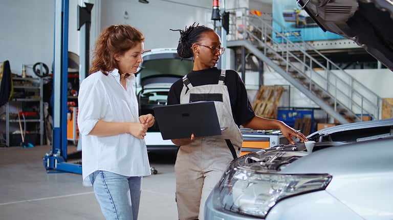 Trained engineer in garage using laptop to follow checklist while doing maintenance on vehicle, talking with client. Worker in car service does checkup on automobile next to customer. Credit: Dragos Condrea 