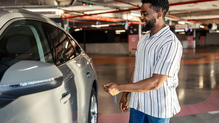 Cheerful young multicultural car driver is locking car door on vehicle in public garage. Credit: dusanpetkovic