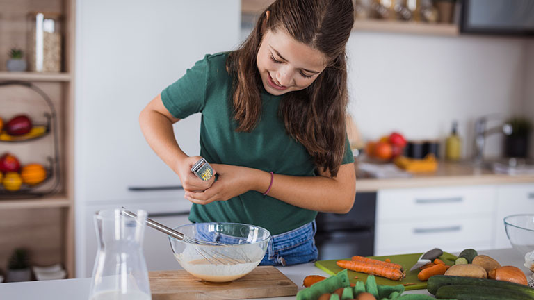 Teenage girl smiling when using garlic press when preparing a meal Credit:Dobrila Vignjevic