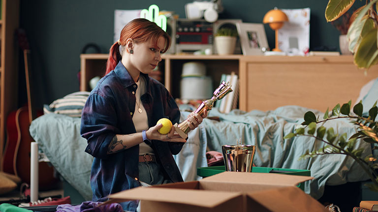 Young Caucasian Woman Packing Trophies and Personal Items in Bedroom Credit: DragonImages
