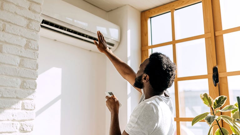 Rear view of young man turning on air conditioner at home Credit: Pekic