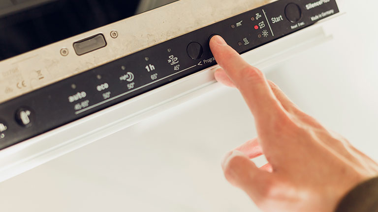 Man choosing eco mode program on the control panel of the dishwasher. By vladdeep