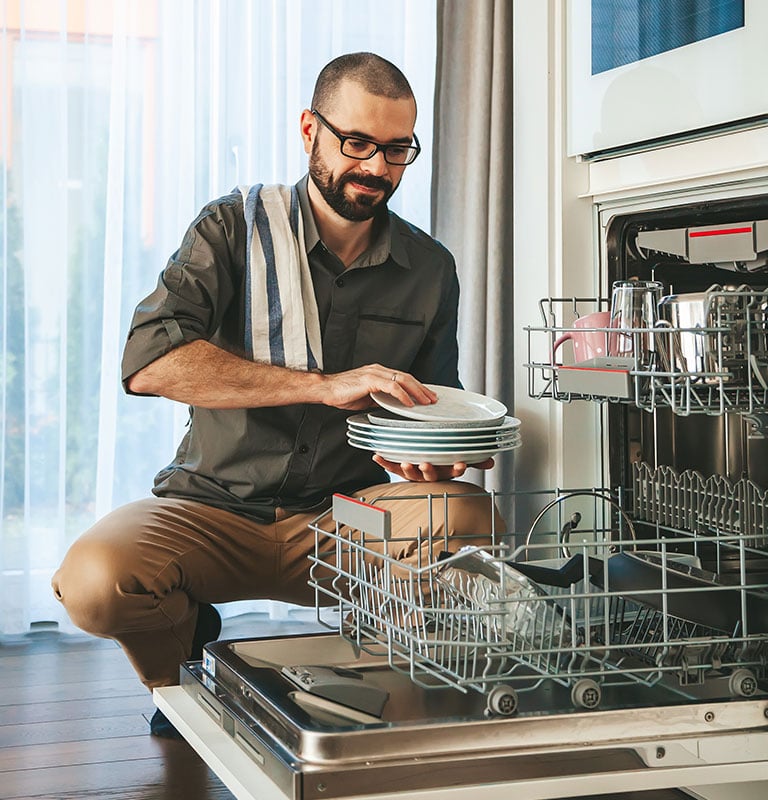 Smiling man unloading dishwasher. By Anna Lurye