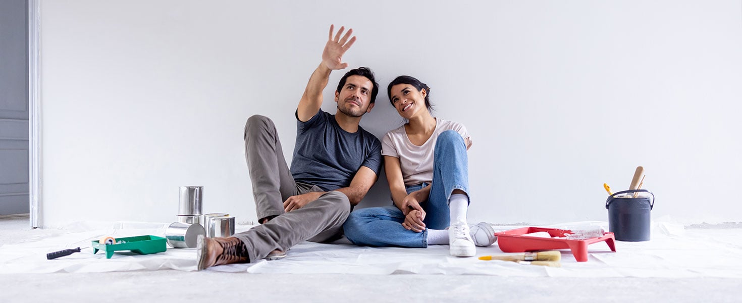 Couple taking a break from painting their house and sitting on the floor sharing ideas and day dreaming; Credit: Hispanolistic