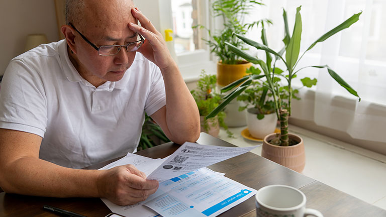 A senior man holding his head trying to cope the raising cost of energy and tax bills. By Ming