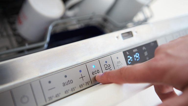 Close Up Of Man Setting Economy Cycle On Dishwasher