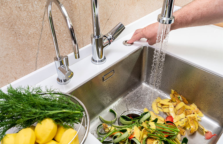 food in sink, person pushing garbage disposal button
