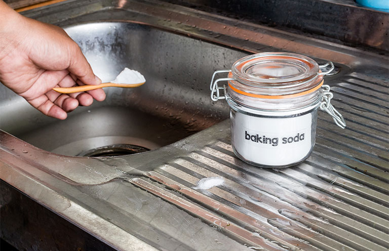 person putting a scoop of baking soda into the sink