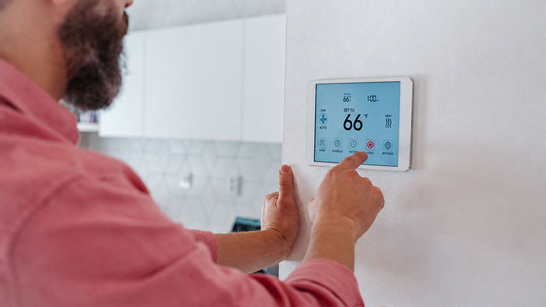 Man using smart thermostat, adjusting or lowering heating temperatures at his home. Concept of sustainable, efficient, and smart technology in home heating and thermostats.