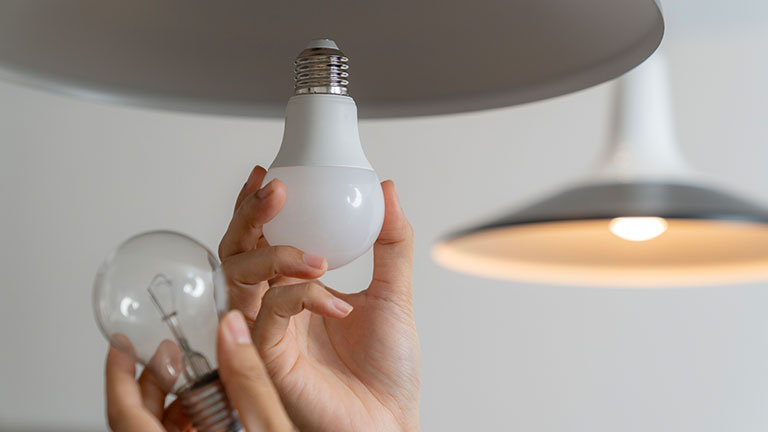A young woman is changing a light bulb from an incandescent bulb to an LED bulb.
