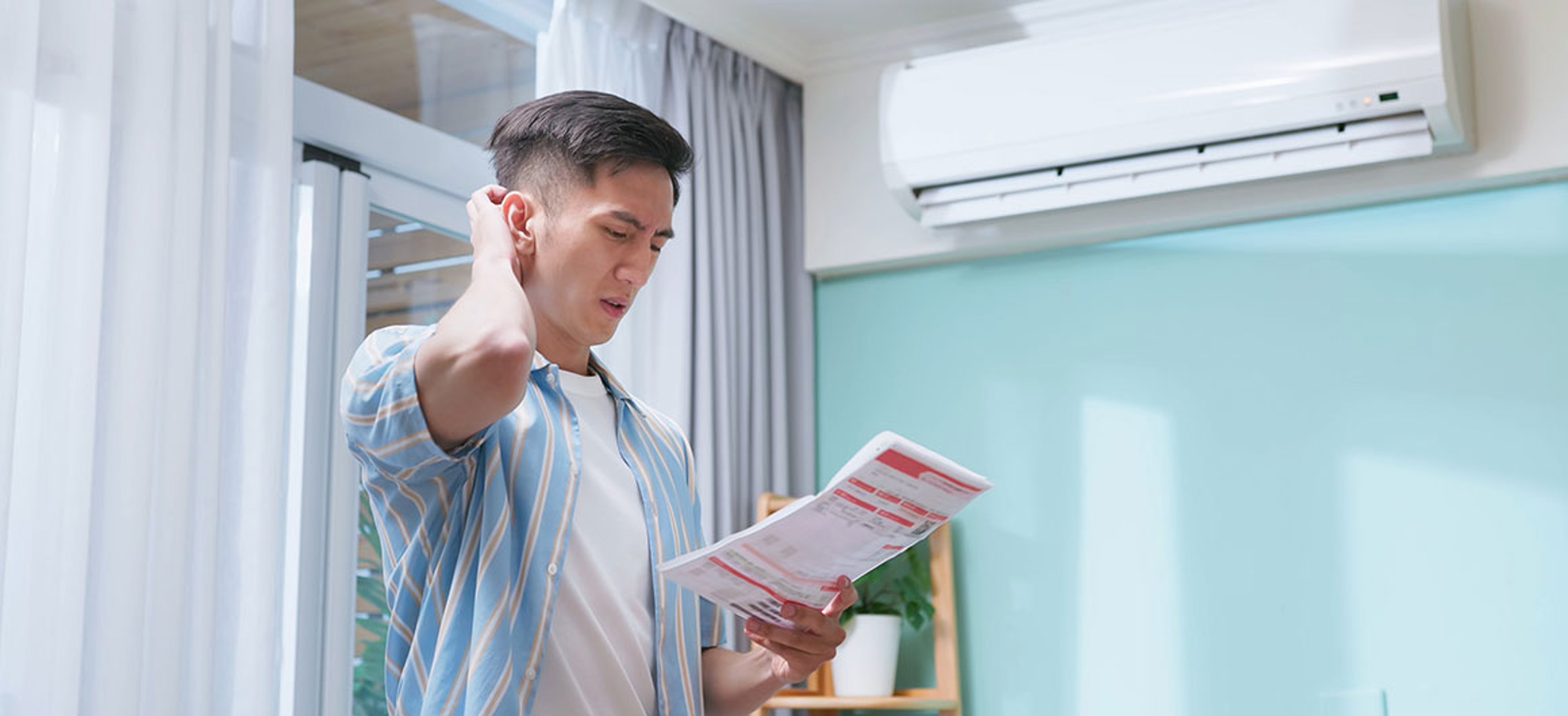 Closeup side view asian man looks at bill in the living room with air conditioner - he feels unhappy because of wasting electricity